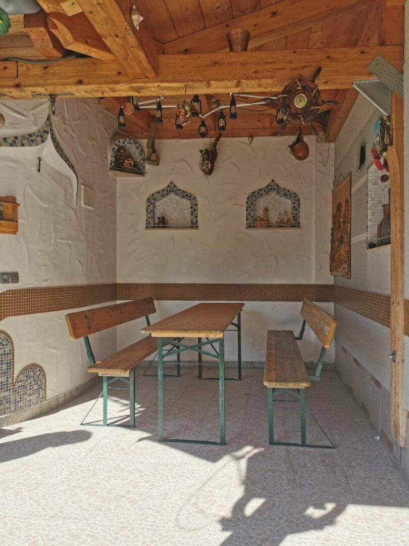 Überdachter Außenbereich mit Holzbalken, rustikalen Bänken und einem Tisch, ideal für gesellige Runden.