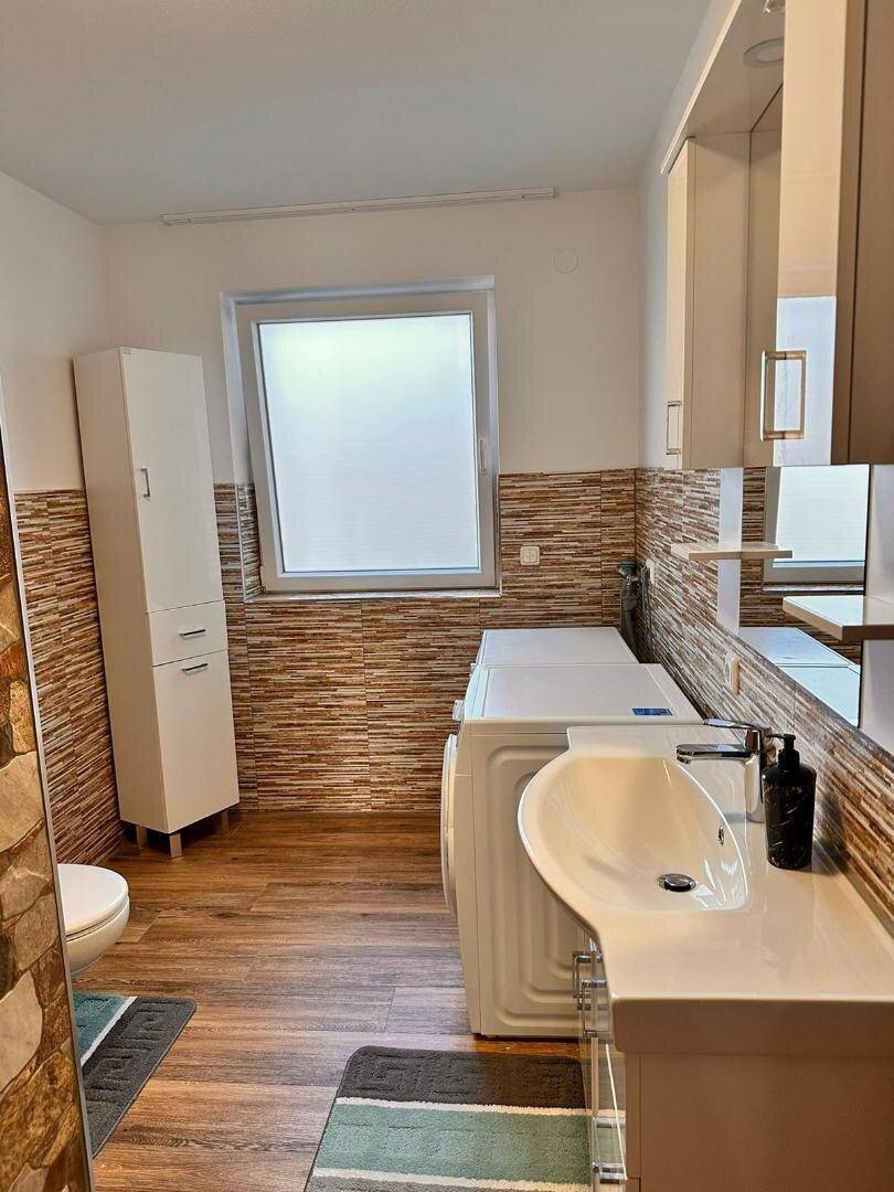 Modernes Badezimmer mit Waschbecken, WC, Waschmaschine und Fenster für Tageslicht.