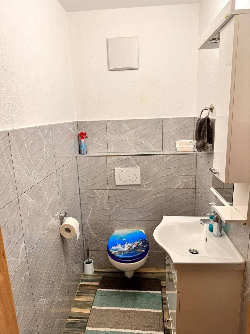 Kleines Gäste-WC mit modernem Waschbecken, Wand-WC und grauen Fliesen.