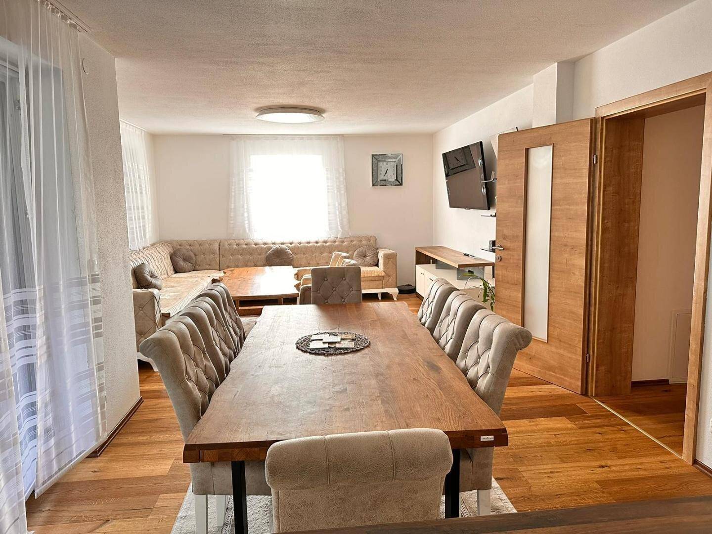 Geräumiger Wohn-Essbereich mit großem Holztisch, bequemer Sitzecke und Parkettboden.