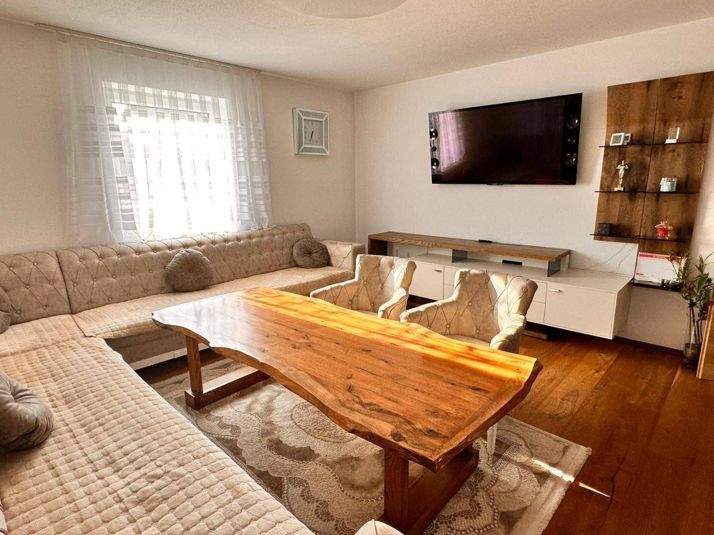 Heller Wohnraum mit großem Flachbildfernseher, bequemer Couch und dekorativem Wandregal.