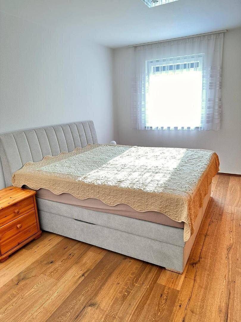 Gemütliches Schlafzimmer mit großem Bett, Holzboden und viel Tageslicht durch das Fenster.