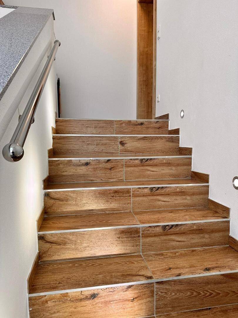 Treppenhaus mit Holzstufen und modernem Edelstahlgeländer, das die Etagen verbindet.