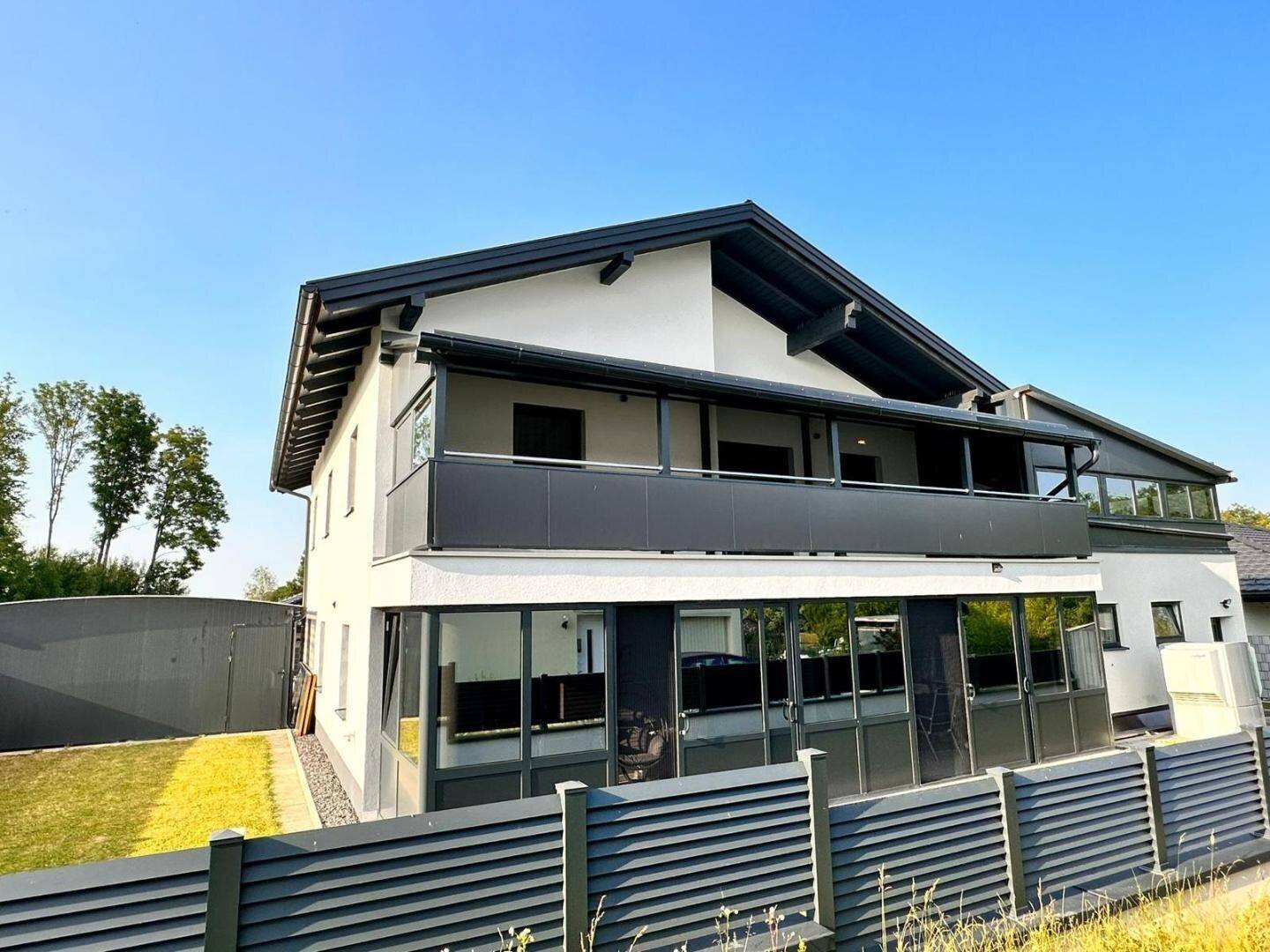 Moderne Hausfassade mit großem überdachtem Balkon und vielen Fenstern.