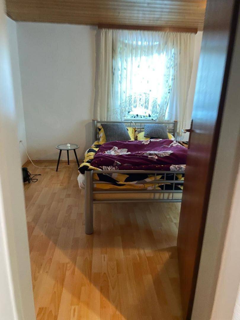 Schlafzimmer mit Doppelbett und Laminatboden, hell durch ein großes Fenster.