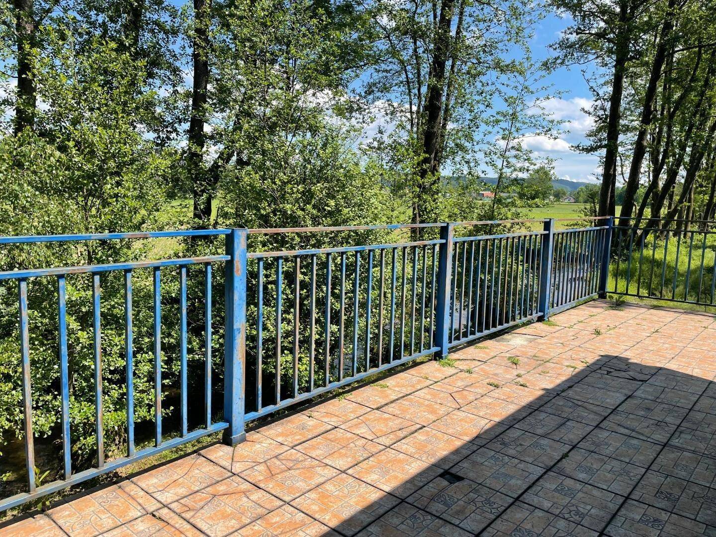 Geflieste Terrasse mit blauem Metallgeländer und weitem Blick auf die grüne Landschaft.