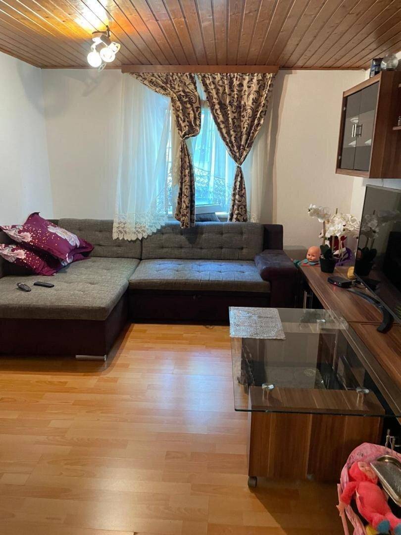 Gemütliches Wohnzimmer mit Ecksofa, Holzdecke und Laminatboden.