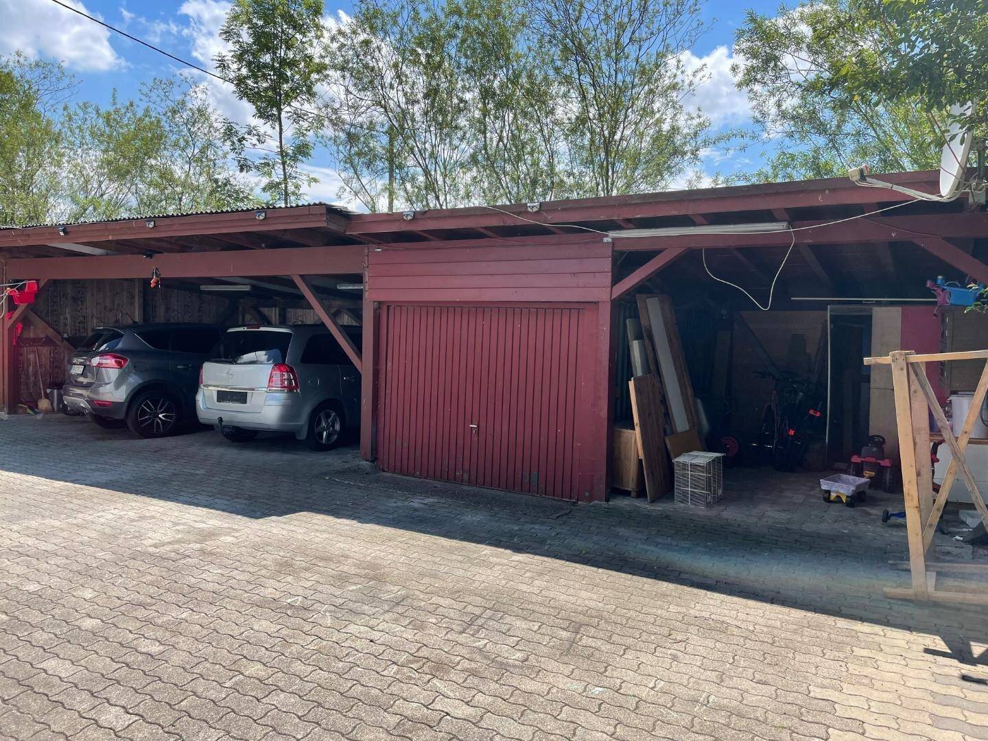 Überdachter Parkplatz mit Holzkonstruktion und separater Garage, gepflasterter Zufahrt.