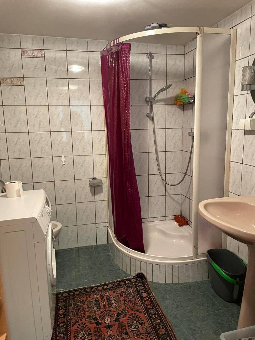 Badezimmer mit Duschkabine, Waschbecken und Waschmaschine, gefliest.