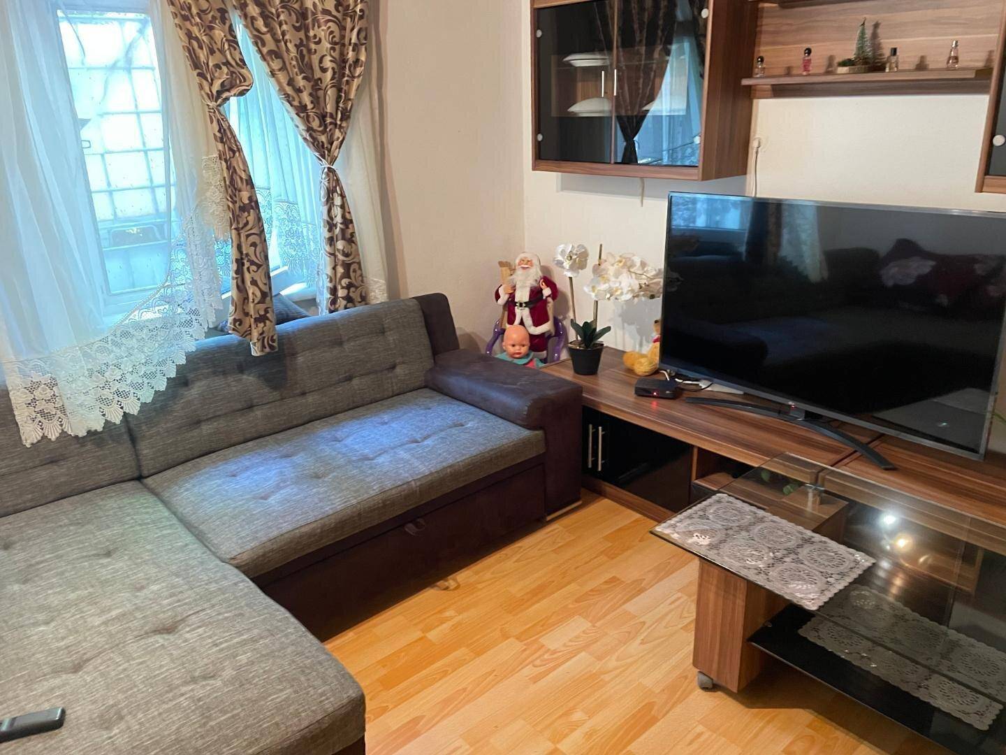 Detailansicht des Wohnzimmers mit Ecksofa, Fernseher und Holzdecke.