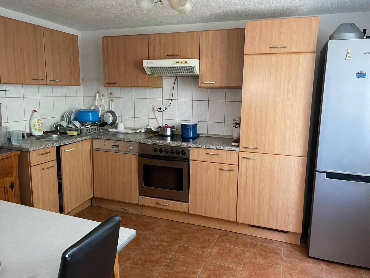 Küche mit hellen Holzschränken, Einbaugeräten und Essbereich mit Tisch.