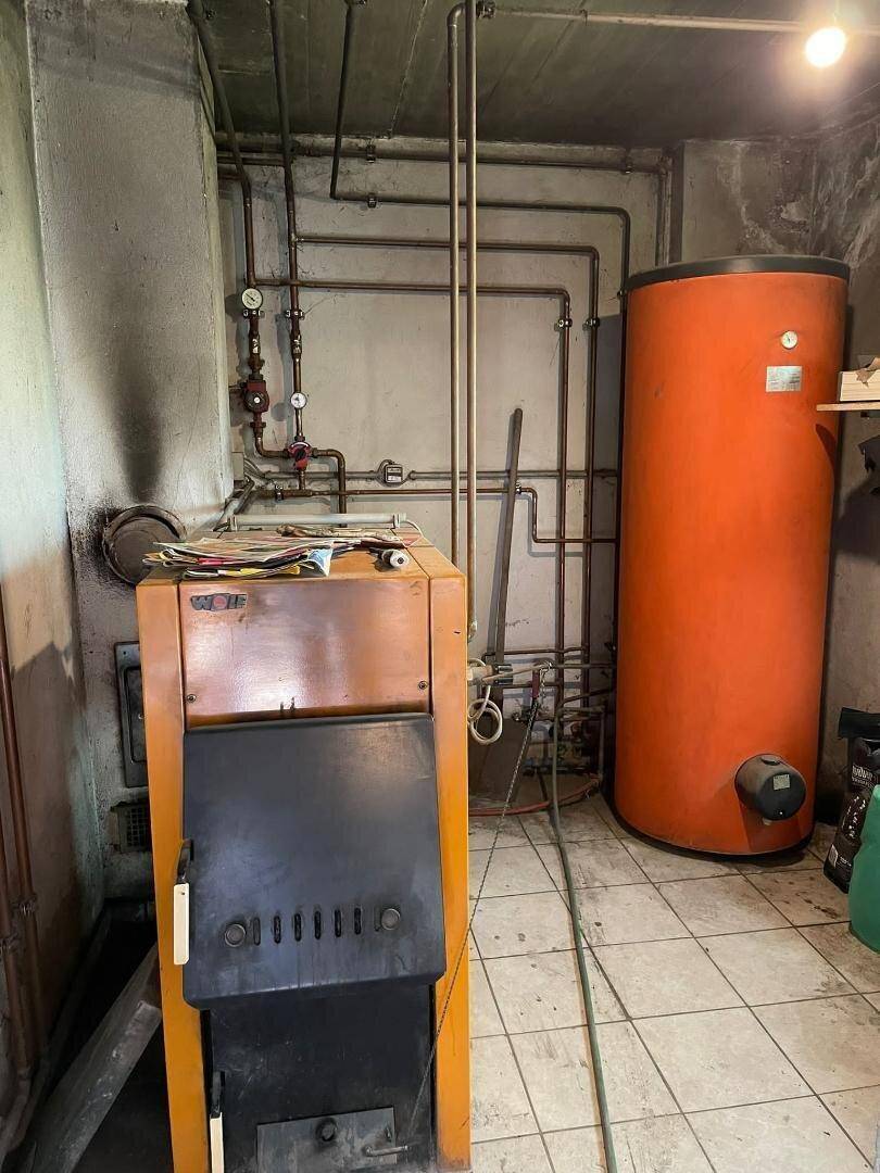 Heizungsraum im Keller mit Kessel, Warmwasserspeicher und sichtbaren Rohrleitungen.