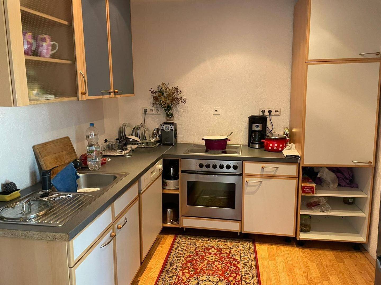 Kleine Küche mit Einbauschränken, Spüle und Kochfeld, Teppich auf Laminatboden.