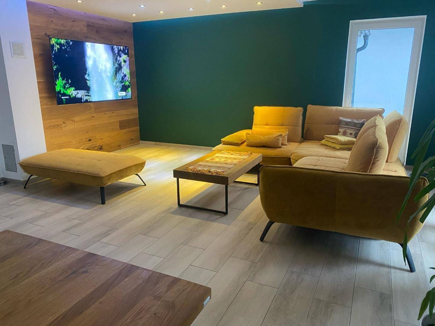 Gemütlicher Wohnbereich mit großem Fernseher an einer Holzwand und bequemen gelben Sofas.