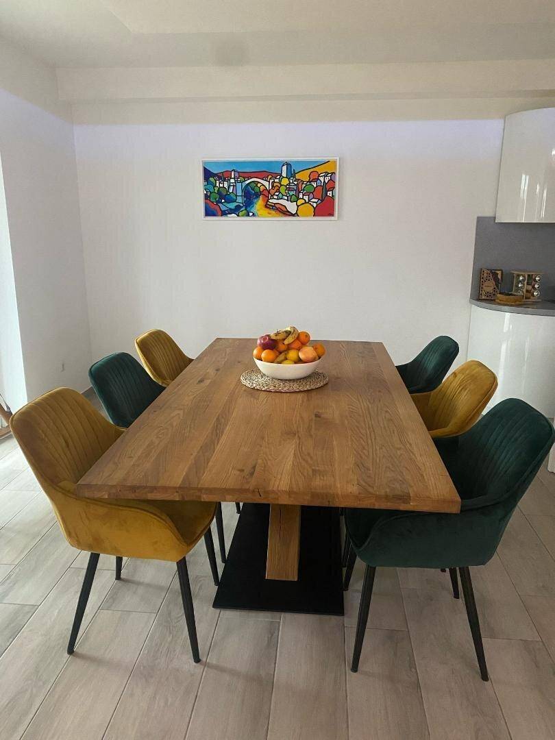Essbereich mit großem Holztisch und farbigen Stühlen, beleuchtet durch natürliches Licht.