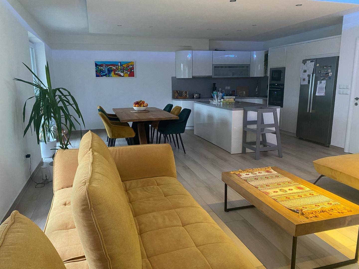 Geräumiger offener Wohn-Essbereich mit moderner Küche, gelben Sofas und viel Tageslicht.