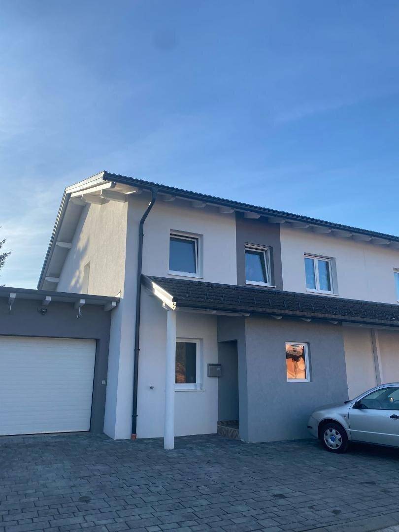 Vorderseite des modernen Hauses mit Garage, gepflasterter Einfahrt und Balkon über dem Eingang.