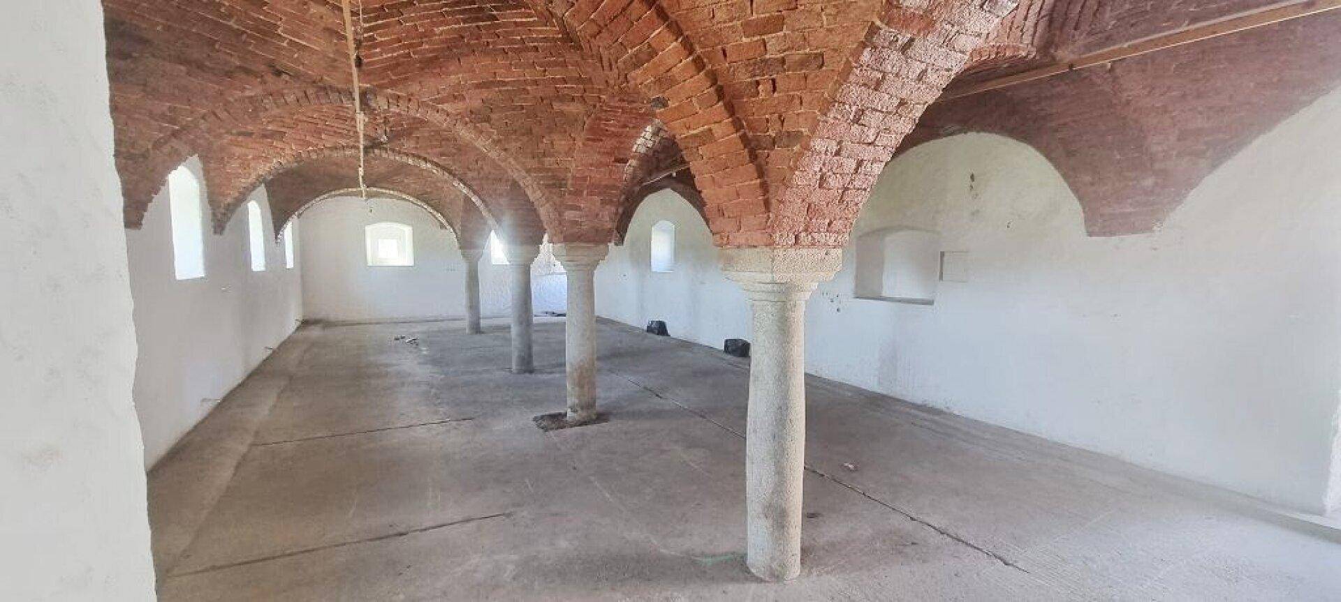 Großer leerer Raum mit beeindruckenden Ziegelgewölbedecken und Betonboden.