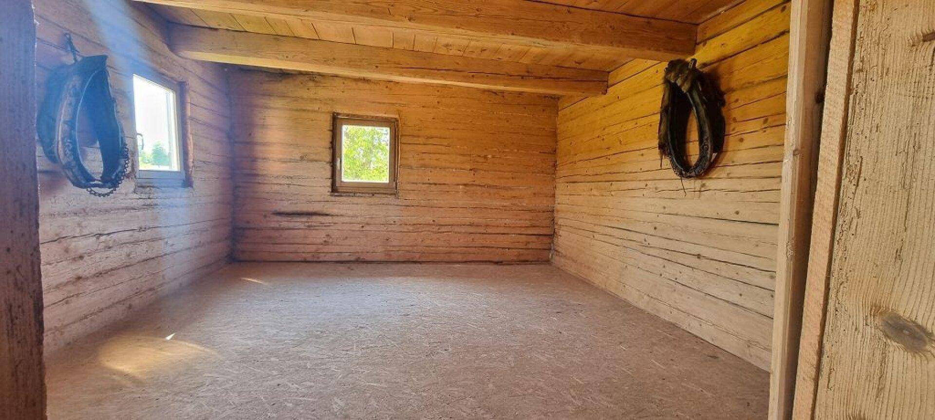 Leerer Raum mit Holzwänden und -decke, kleinen Fenstern und rustikalem Charme.