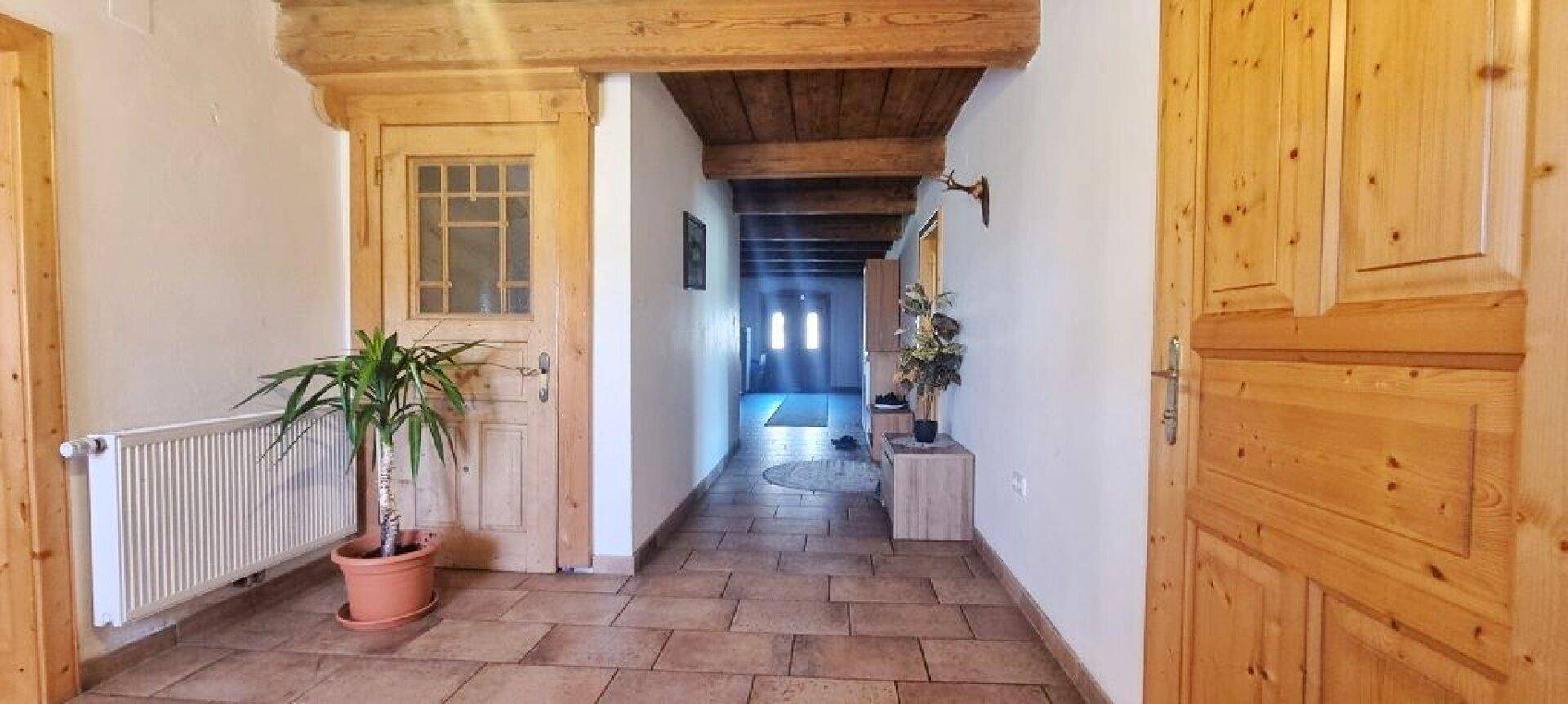 Rustikaler Flur mit Holztüren, Terrakotta-Fliesenboden und sichtbaren Holzdeckenbalken.
