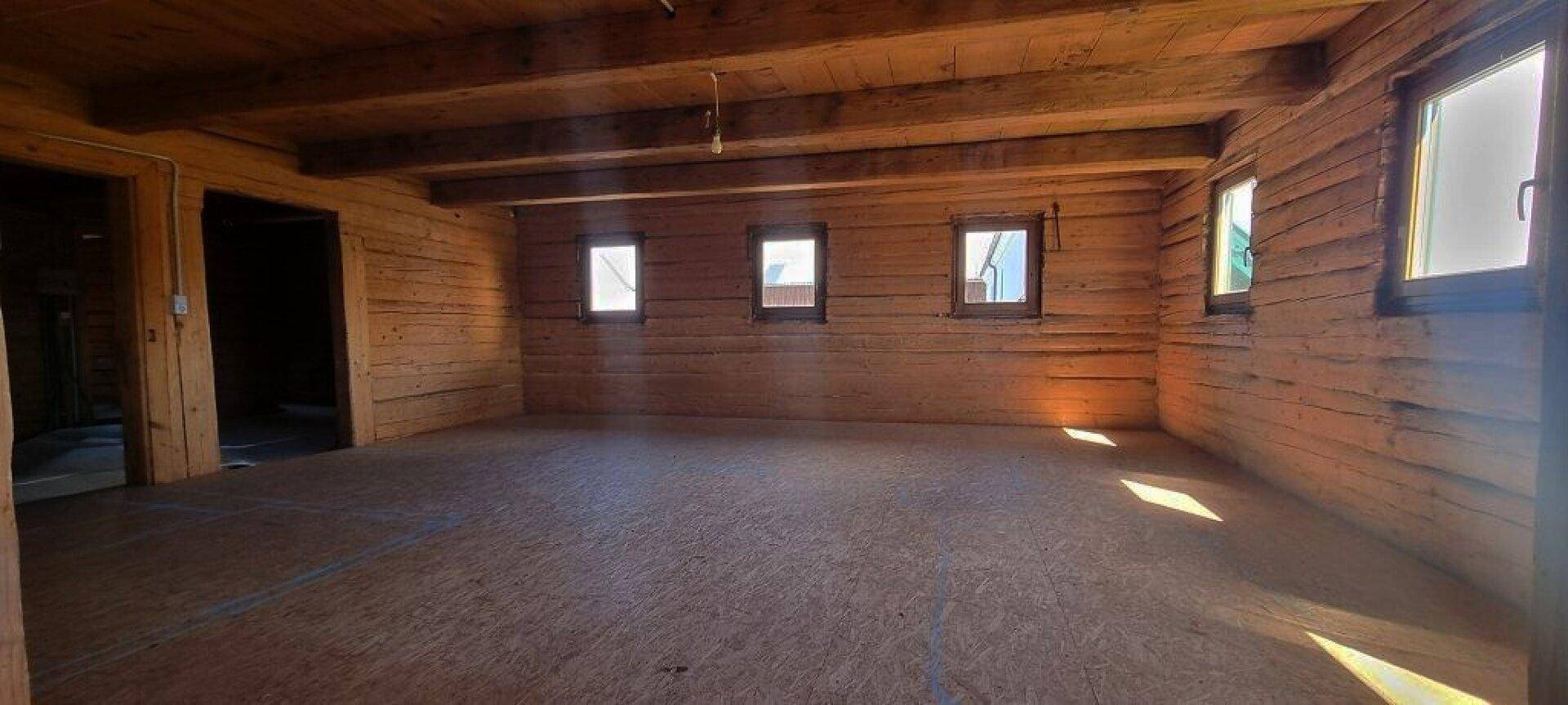 Heller, leerer Raum mit Holzwänden und -decke, vielen kleinen Fenstern.