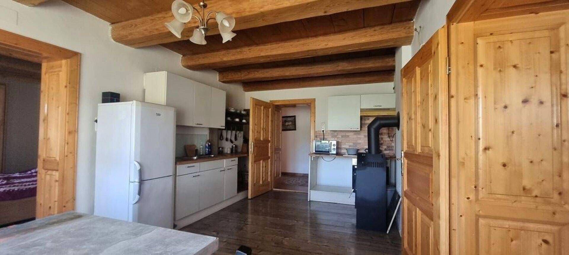 Gemütliche Küche mit weißen Schränken, Kühlschrank und einem traditionellen Holzofen.