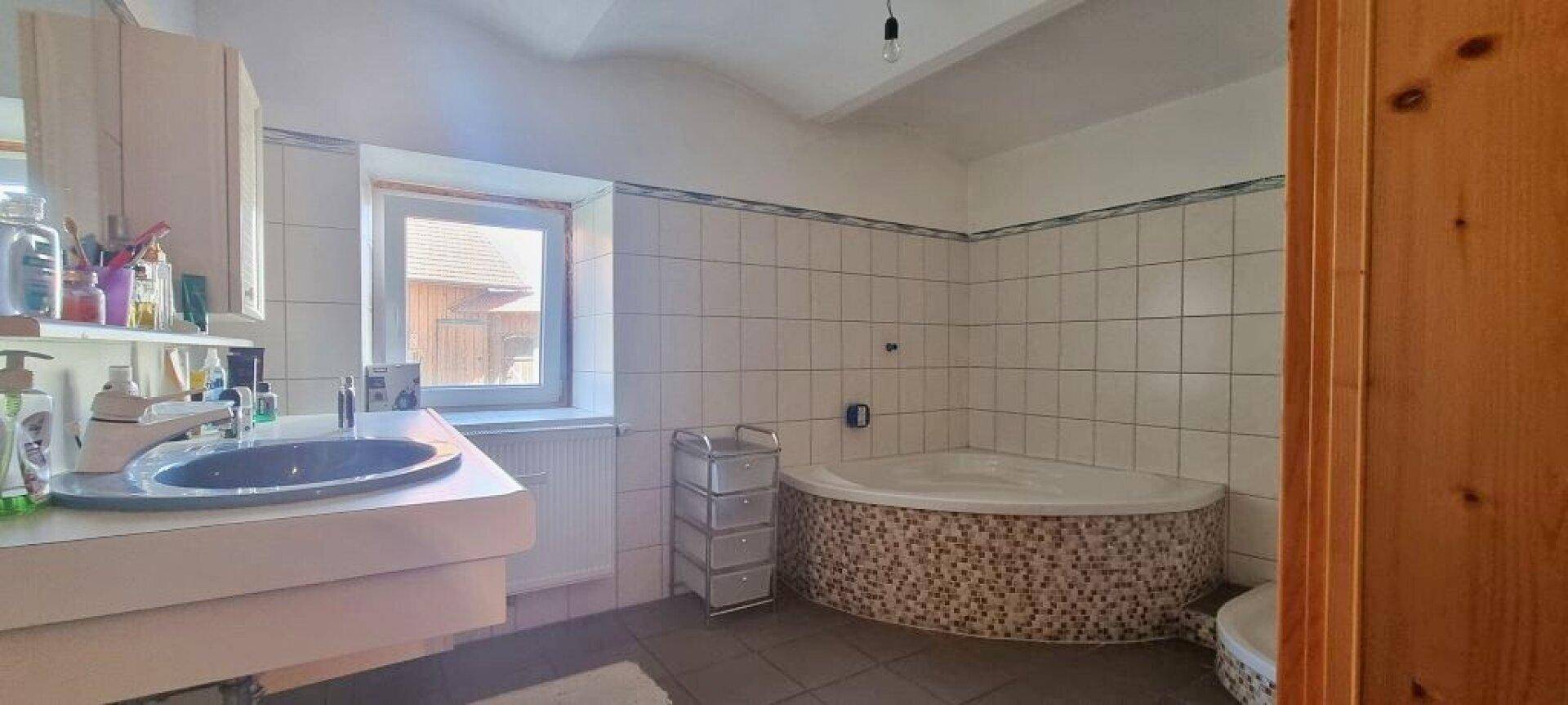 Badezimmer mit Eckbadewanne, Waschbecken und hell gefliesten Wänden.