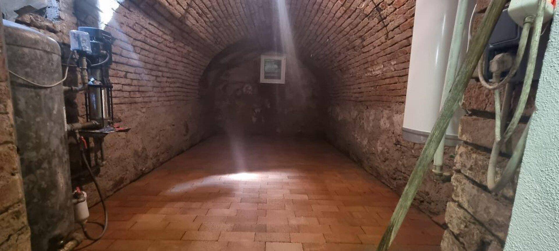 Historischer Keller mit Ziegelgewölbe, Fliesenboden und sichtbaren Installationen.