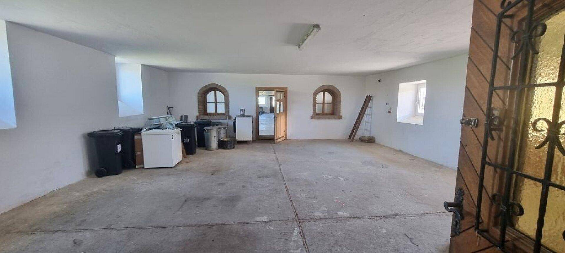 Großer, leerer Raum mit Betonboden, Rundbogenfenstern und Abfallbehältern.