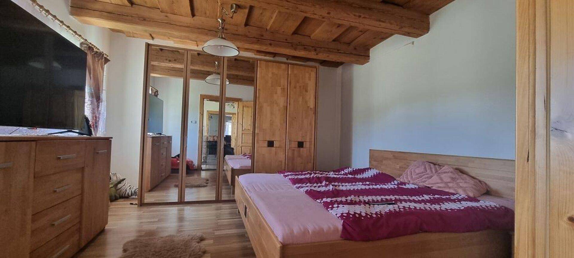 Schlafzimmer mit Holzbett, großem Spiegelschrank und rustikalen Holzdeckenbalken.