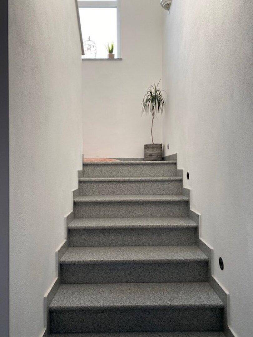 Heller Treppenaufgang mit grauen Stufen und einem kleinen Fenster für natürliches Licht.