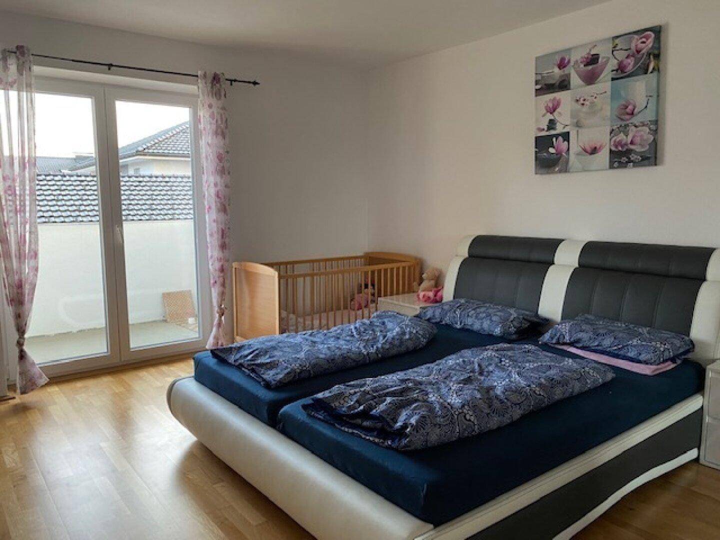 Helles Schlafzimmer mit Holzboden und Zugang zu einem Balkon, ideal für Familien.