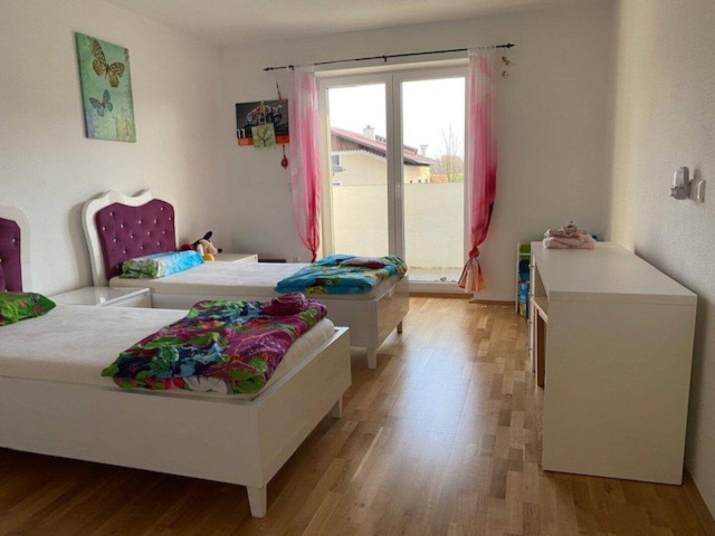 Farbenfrohes Kinderzimmer mit zwei Einzelbetten, Holzboden und Zugang zu einem Balkon.