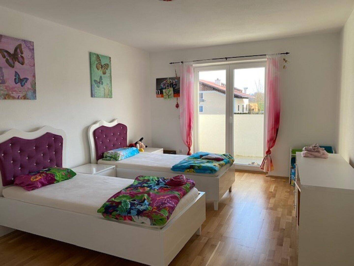 Geräumiges Kinderzimmer mit Holzboden, bunten Akzenten und Zugang zu einem sonnigen Balkon.