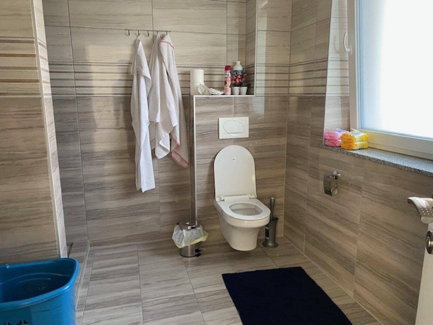 Modern gefliestes Badezimmer mit Toilette und einem Fenster für natürliche Belüftung und Licht.