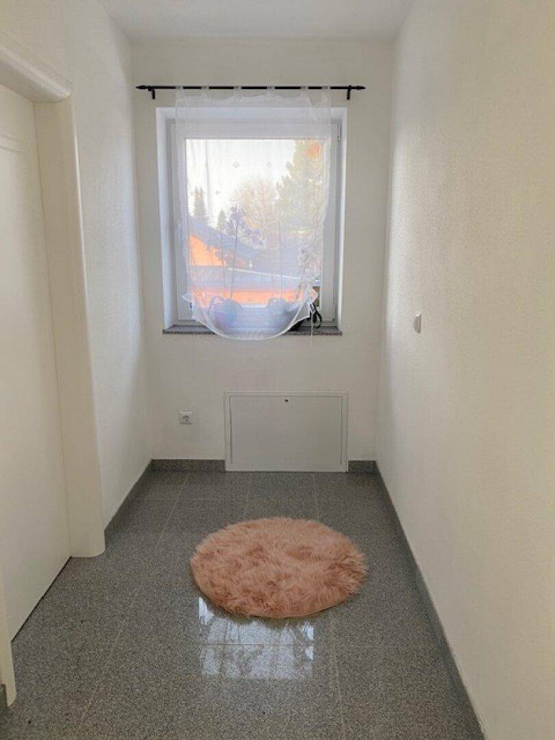 Heller Flur mit einem Fenster, das für ausreichend Tageslicht sorgt, und einem weichen Teppich.
