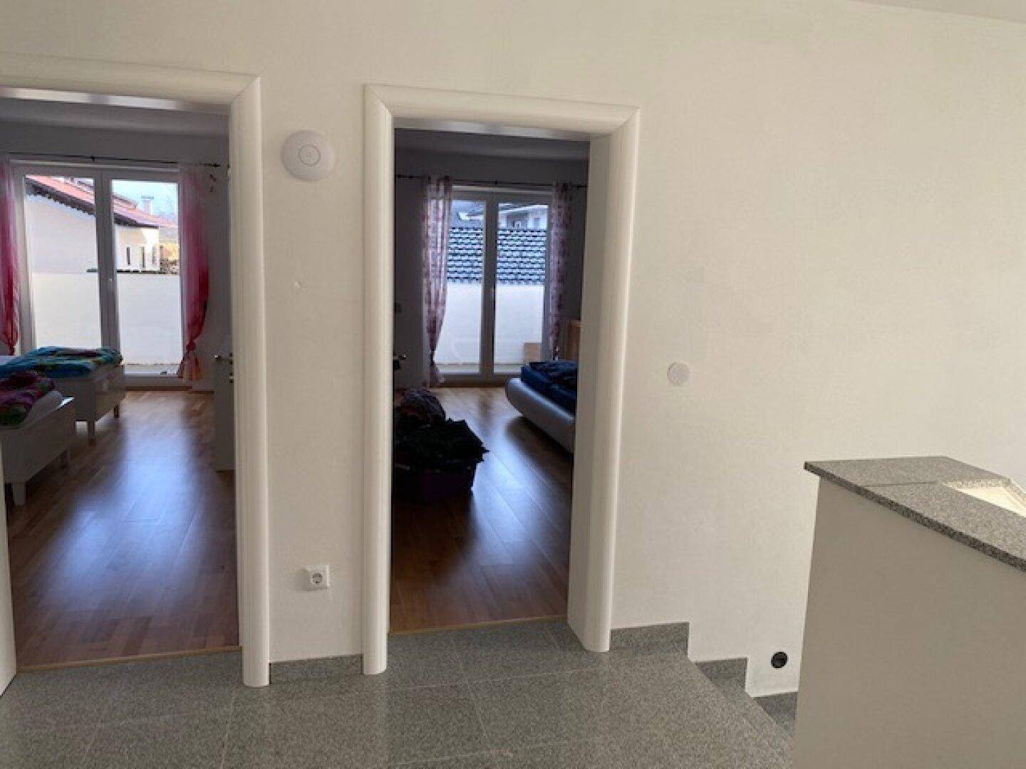 Blick vom Flur in zwei helle Schlafzimmer mit Holzböden und Zugang zu den Balkonen.