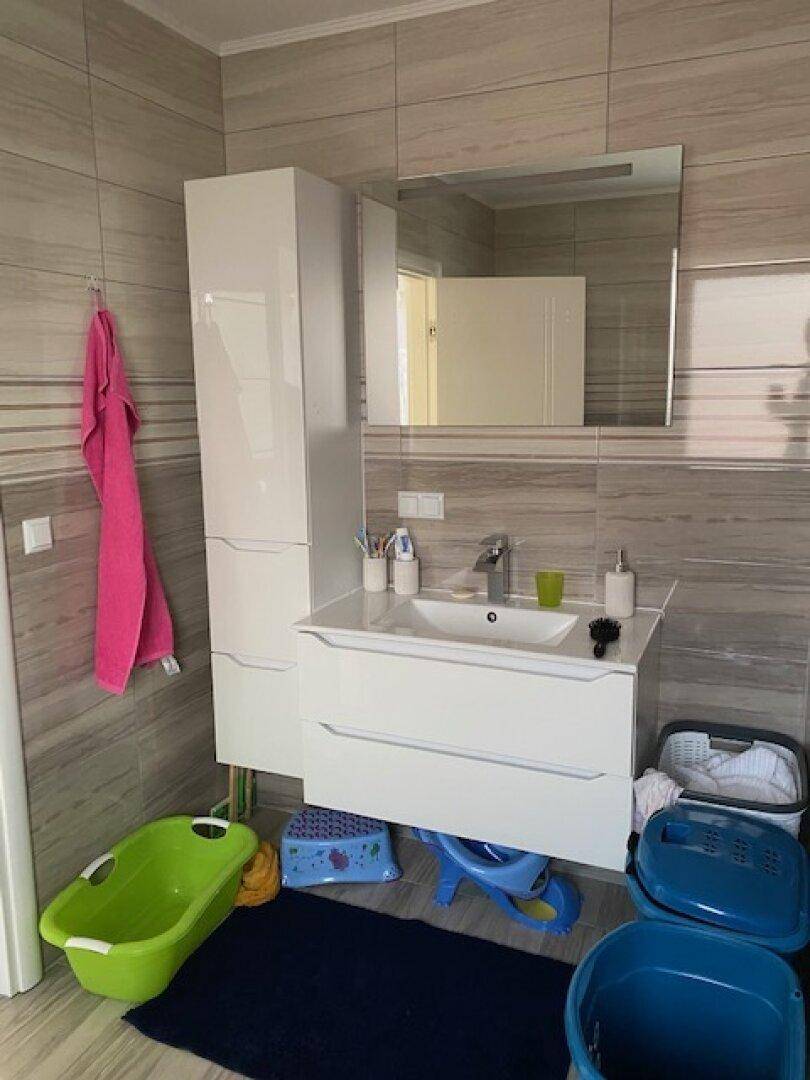 Badezimmer mit modernem Waschtisch, Spiegel und praktischem Hochschrank für zusätzlichen Stauraum.