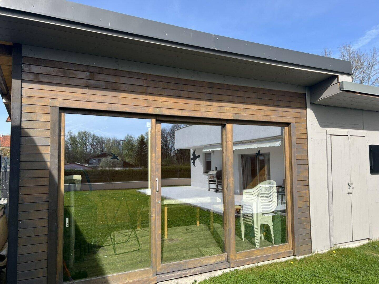 Moderne Holzfassade mit großen Glasschiebetüren und Blick auf den Garten mit Terrasse.