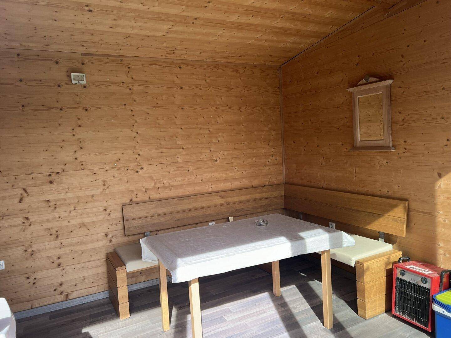 Gemütlicher Essbereich mit Holzwänden, Holzbänken und einem Tisch mit weißer Decke.