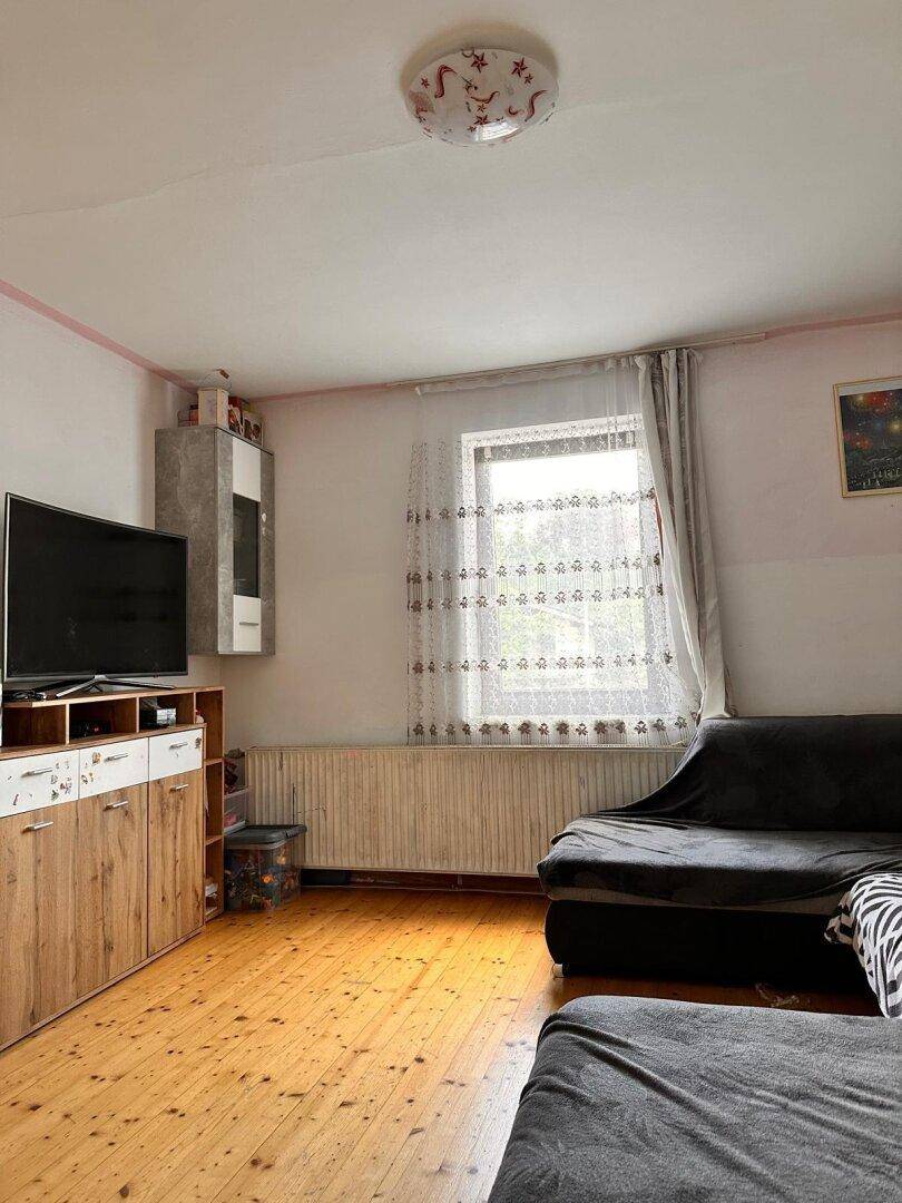 Gemütliches Wohnzimmer mit Sofa, TV-Möbel und einem Fenster mit Vorhang.