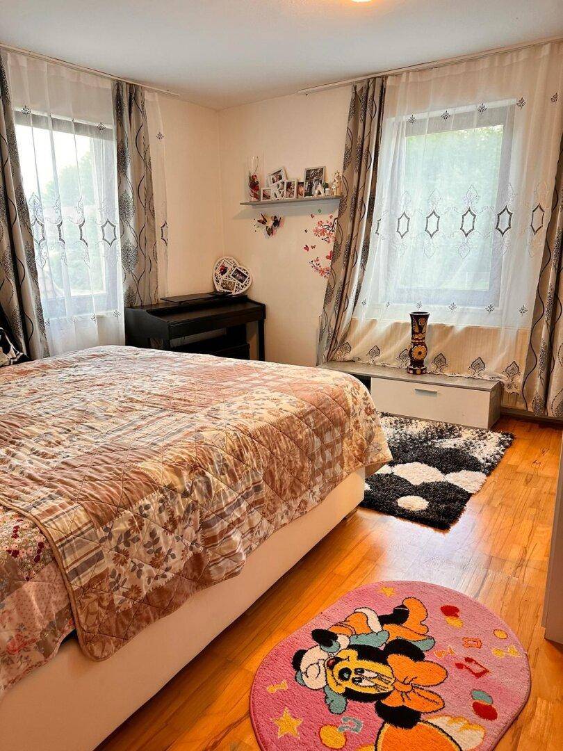 Helles Schlafzimmer mit Doppelbett, Holzboden und zwei großen Fenstern.