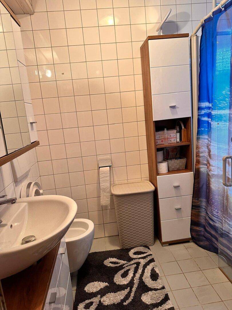 Badezimmer mit Waschbecken, Toilette, Duschkabine und weißen Wandfliesen.