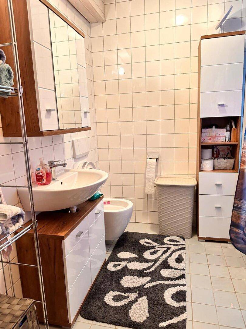 Badezimmer mit Waschbecken, Spiegelkabinett und weißen Wandfliesen.