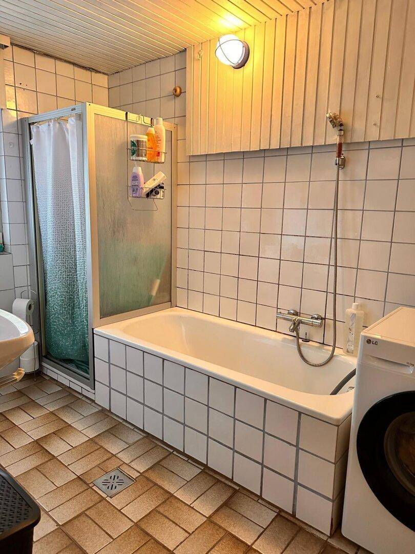 Badezimmer mit Badewanne, Duschkabine und Waschmaschine, gefliestem Boden.