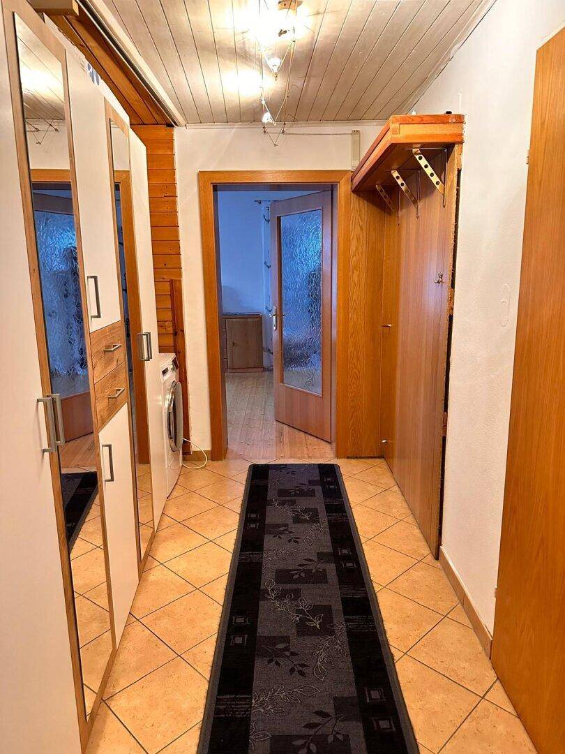 Langer Flur mit Spiegelschränken, Fliesenboden und Holzakzenten an der Decke.