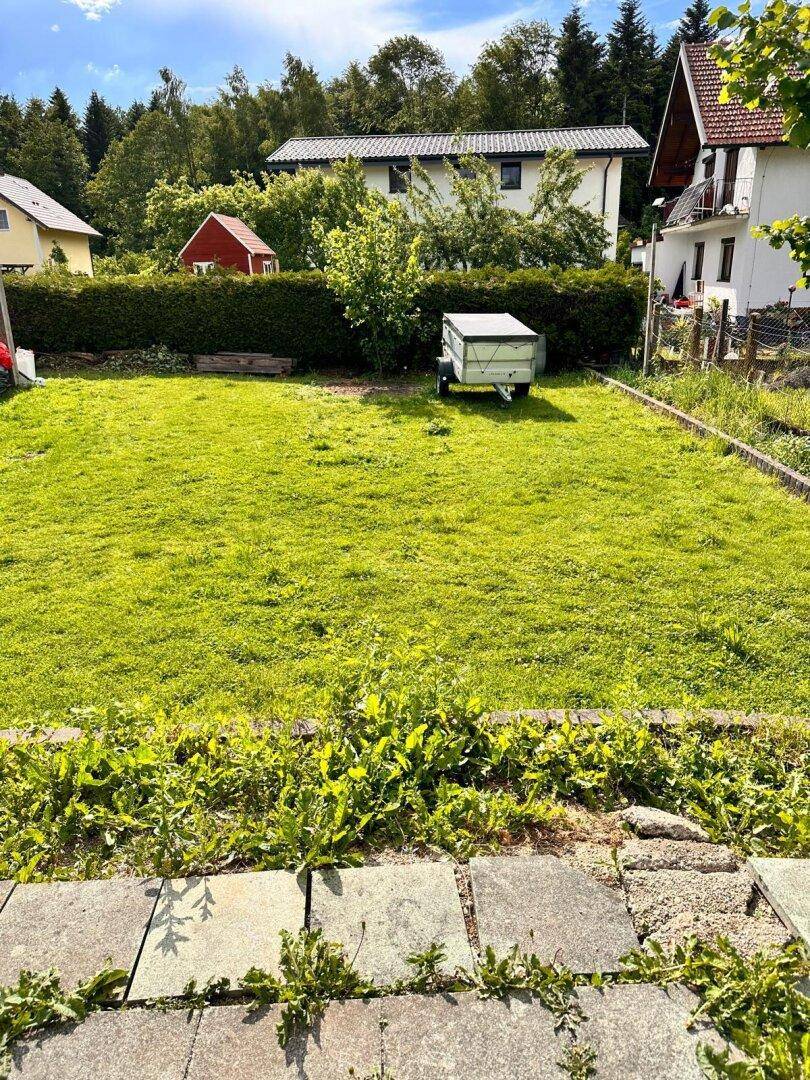 Weitläufige Rasenfläche im Garten mit einem kleinen Anhänger.