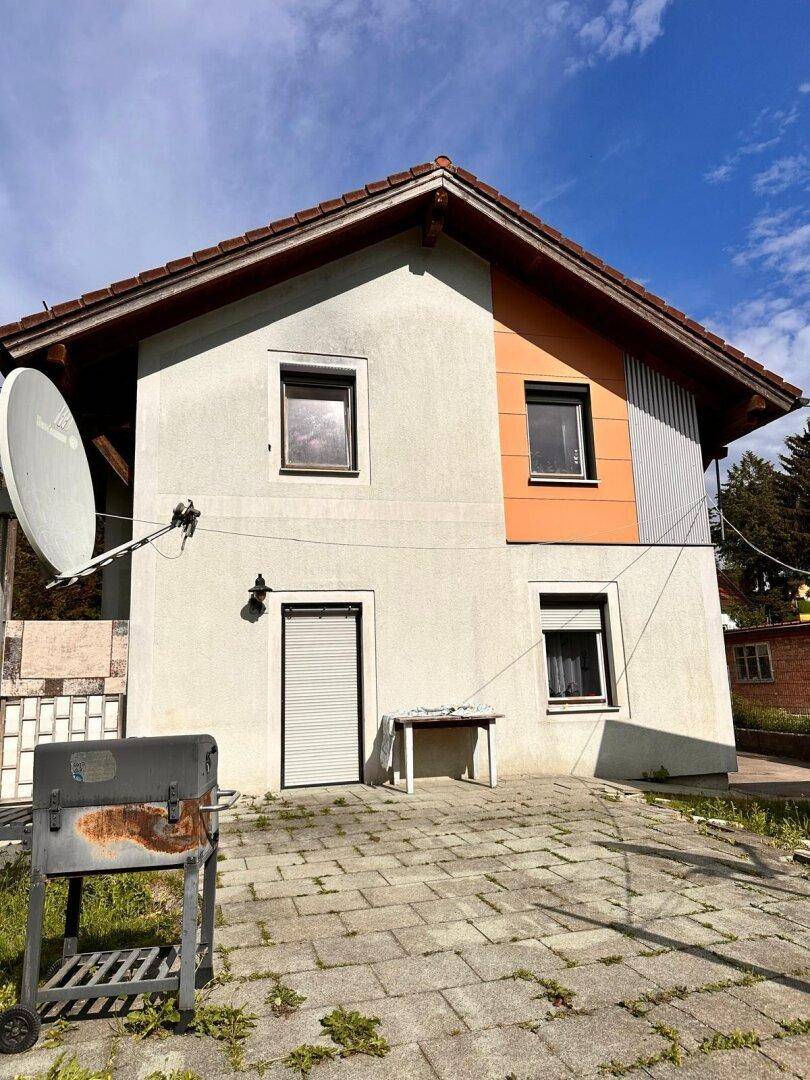 Außenbereich mit gepflasterter Terrasse, Grill und Blick auf das Haus.