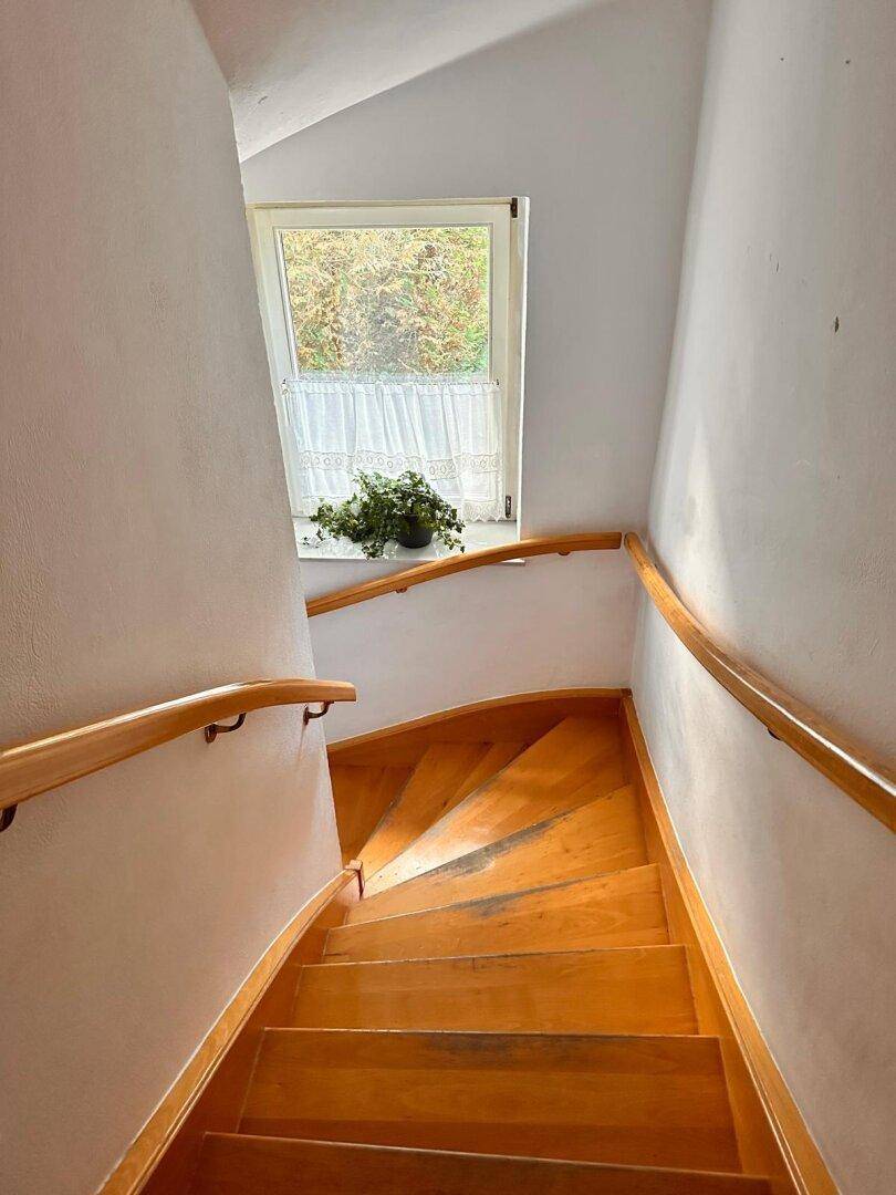 Holztreppe mit Handlauf und Fenster, die die verschiedenen Etagen verbindet.