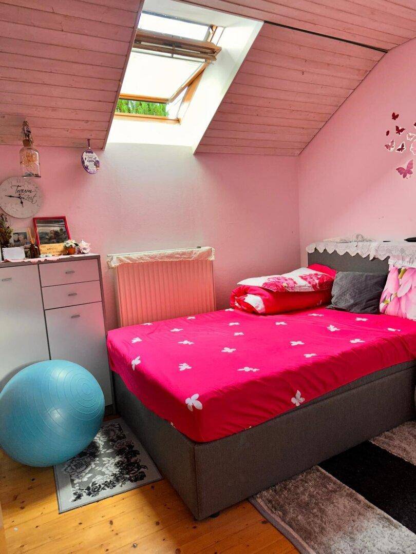 Rosa Schlafzimmer im Dachgeschoss mit Bett, Dachschräge und Dachfenster.